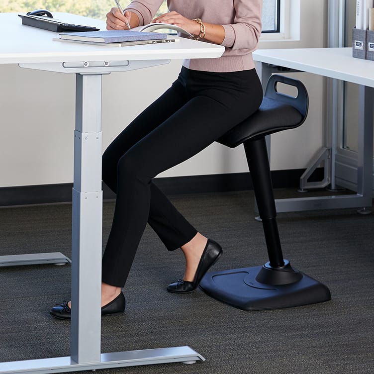 professional seated on active seat and working on electric standing desk