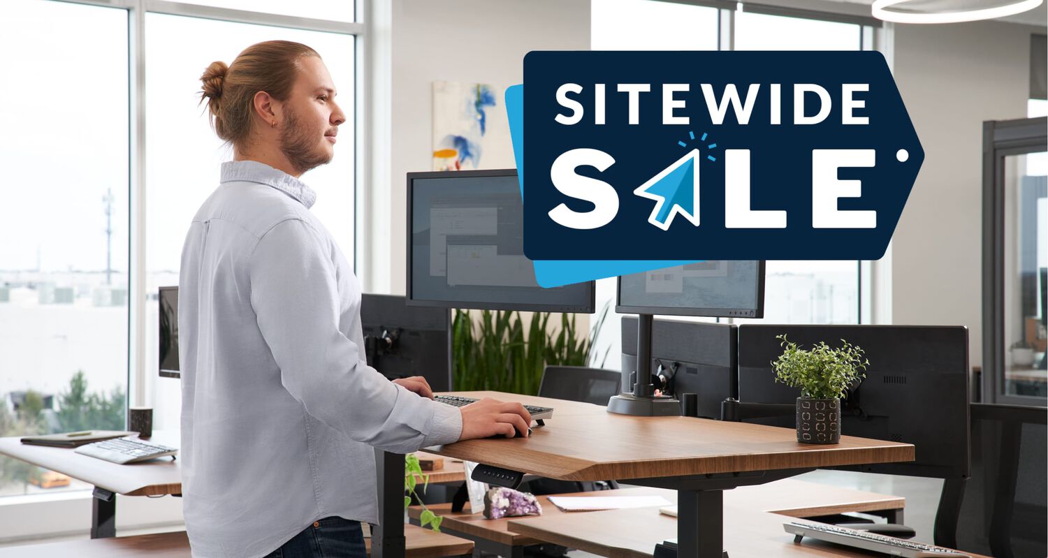 individual working at a desk in an office setting with the words sitewide sale above the monitors